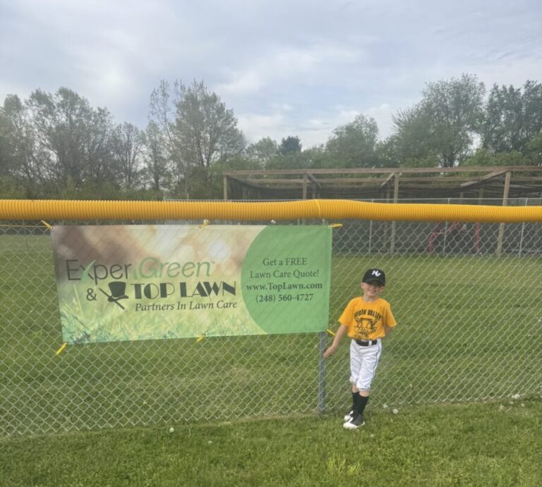 T-Ball player next to Top Lawn banner.
